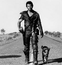 a man is walking down the road with a dog in his hand and wearing leather gear