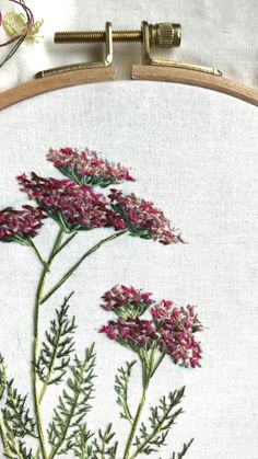 a close up of a embroidery on a white cloth with pink flowers and green leaves