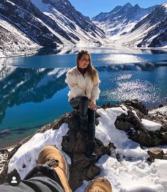 a woman sitting on top of a snow covered mountain next to a lake