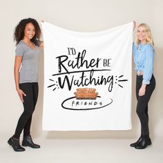 two women holding up a white banner that says i'd rather be watching friends