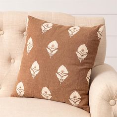 a brown and white pillow sitting on top of a couch next to a beige chair