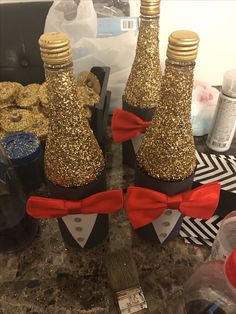 two wine bottles with red bow ties and gold glitter on them are sitting on a counter