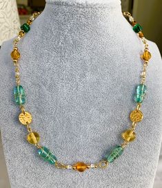 Stunning Art Deco-inspired necklace handmade with vintage-style Czech glass beads and gold-plated findings. This 17.5-inch necklace features a beautiful combination of gold, blue, green, yellow, orange, and translucent beads that are sure to catch the eye of everyone in the room. The large blue beads are even wire-wrapped, adding an extra touch of elegance and texture. The necklace is perfect for women who want to make a statement with their accessories, whether it's for a special occasion or ju Gold Beaded Necklaces With Czech Glass, Unique Gold Beaded Necklaces With Spacer Beads, Unique Gold Wire Wrapped Beaded Necklace, Gold Czech Glass Beaded Necklace With Colorful Beads, Gold Beaded Necklace With Colorful Czech Glass, Gold Necklace With Wire Wrapped Round Beads, Gold Glass Jewelry Wire Wrapped, Adjustable Gold Wire Wrapped Beaded Necklaces, Green Wire Wrapped Beaded Necklaces With Round Beads