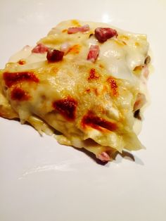 a piece of pizza with cheese and ham on it sitting on a white plate, ready to be eaten