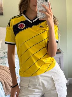 a woman taking a selfie with her cell phone in front of her face while wearing a yellow shirt and white shorts