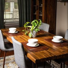 a dining room table with plates and bowls on it, in front of a window