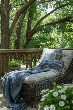 a wicker chaise lounge on a deck with blue and white throw pillows, potted plants and trees in the background