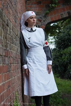 a woman in a white dress leaning against a brick wall with a red cross on it