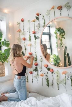 a woman standing in front of a mirror with flowers on the wall