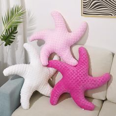 three pink and white starfish pillows sitting on a couch in front of a plant