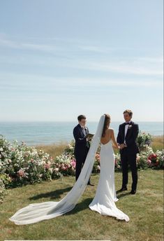 a bride and groom standing next to each other on top of a grass covered field