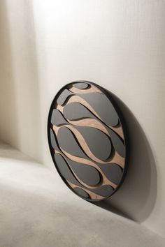 a black and brown circular object hanging on the wall next to a white wall with light coming through it