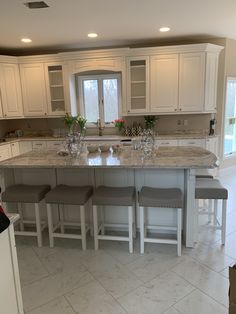 a large kitchen with marble counter tops and white cabinets, along with four stools