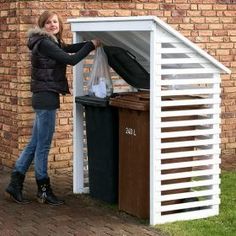 a woman standing next to a building with a trash can in front of it and a garbage can behind her