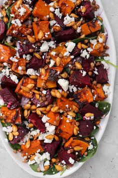 a white platter filled with roasted beets, feta cheese and pine nuts