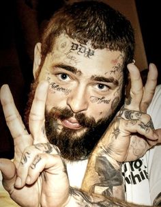 a man with lots of tattoos on his face making the peace sign and holding his hands up in front of him