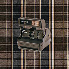 an old polaroid camera sitting on top of a plaid wall