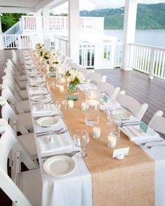 a long table is set up with white chairs and place settings for an outdoor dinner