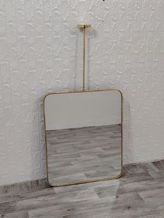 a mirror sitting on top of a wooden floor next to a white wall with a gold frame