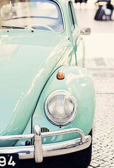 the front end of an old green car parked on a cobblestone street in europe