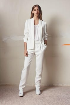 a woman standing in front of a wall wearing white pants and a blazer jacket