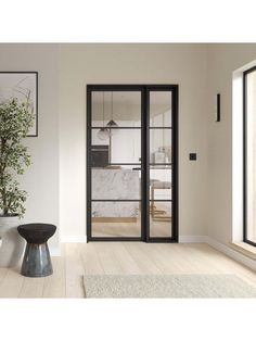 an empty living room with white walls and wood floors, black glass doors and a potted plant in the corner