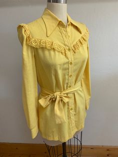 "Sweet yellow blouse, designed to be worn untucked, with a tie at waist that can be tied in front or back. Sweet crochet lace trim at cuffs and yoke. Western detailing. Not sure of the fiber content but it feels like a poly blend, but it has the look of a raw silk loose weave. Laid flat it measures- Shoulder to shoulder 14.5\" Pit to pit 19\" Neck 8\" Waist 16\" Hip 19\" Front length 26\" Model is 5'8\" size 6 for reference Please ask any questions prior to purchase and see all photos, all sales Fitted Long Sleeve Blouse With Crochet Trim, Yellow Tops With Crochet Trim For Spring, Vintage Tie Neck Tops For Spring, Vintage Crochet Trim Tops For Spring, Spring Crochet Trim Blouse, Fitted Yellow Blouse For Daywear, College Clothes, Blouse Designed, Crochet Lace Trim