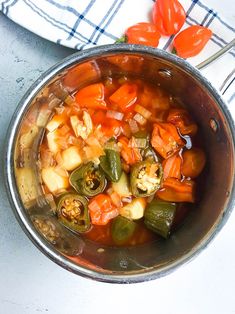 a metal bowl filled with vegetables on top of a white tablecloth next to tomatoes