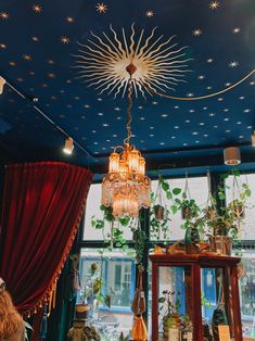 a chandelier hanging from the ceiling in a room with red curtains and potted plants