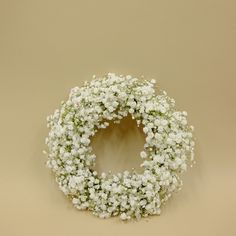 a white wreath with baby's breath hanging from the side on a tan wall