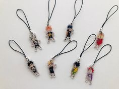 six necklaces with little cartoon characters hanging from black cords on a white table top