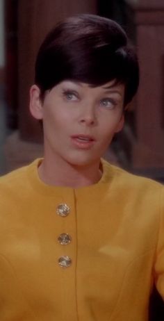 a woman with short black hair wearing a yellow shirt and gold buttons on her collar