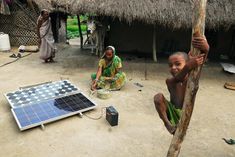 two children playing with a solar panel in front of a hut on the ground,