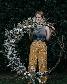 a woman standing in front of a bush holding a twig with flowers on it