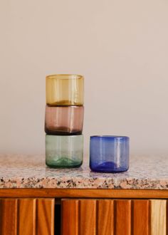 three different colored glass cups sitting on top of a wooden cabinet next to each other