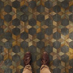 a person's feet in brown shoes standing on a tiled floor with wooden blocks