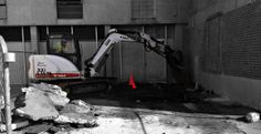 an excavator digging through rubble in front of a building