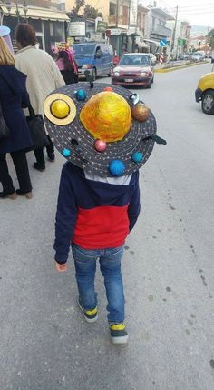 a little boy walking down the street wearing a hat with planets on it