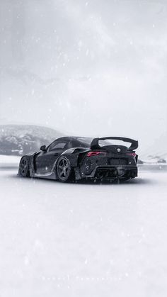 a black sports car parked on top of a snow covered field with mountains in the background