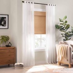 a living room with white curtains and a brown chair in front of a large window