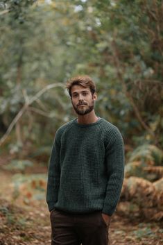 a man standing in the middle of a forest wearing a green sweater and brown pants