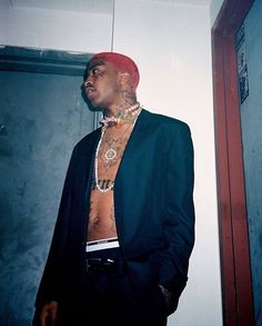 a man in a black suit with tattoos on his chest and shirtless torso standing next to a door