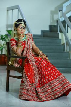 a woman sitting in a chair wearing a red and white bridal outfit with gold jewelry