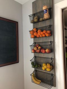 three metal baskets filled with fruit on top of a wooden shelf next to a chalkboard