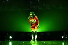 a man standing on top of a stage holding a microphone in his hand and wearing an orange shirt