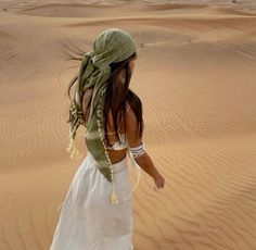 a woman in a white dress and green scarf walking through the desert with sand dunes behind her