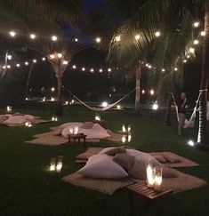 an outdoor area with lights and blankets on the grass, surrounded by palm trees at night