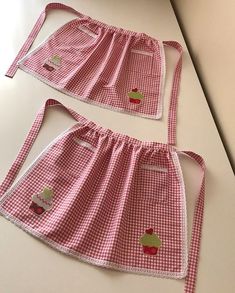 two aprons with apple applique on them sitting on a counter top next to each other