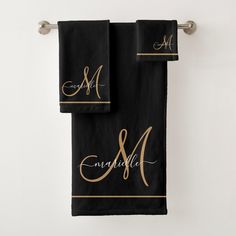 two black towels with gold monogramming and the letter m on them are hanging from a towel rack