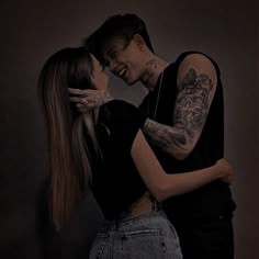 two people standing next to each other with tattoos on their arms and shoulders, one person kissing the other